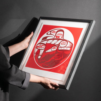 Model holding Framed Killer whale and Salmon fine Art print by renowned Haida Artist, Robert Davidson on a black background