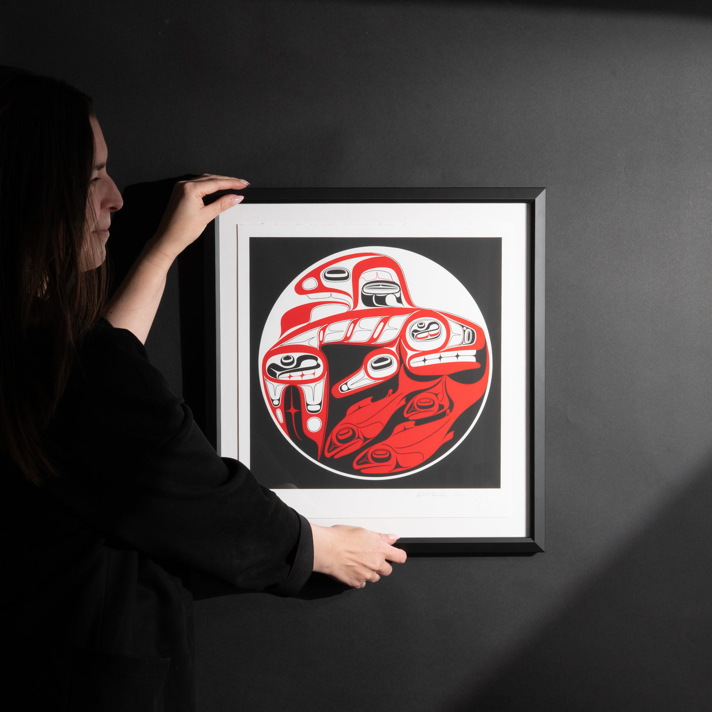 Model admiring Framed Killer whale and Salmon fine Artist proof by renowned Haida Artist, Robert Davidson on a black background