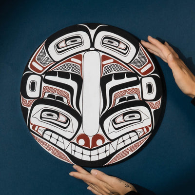 Hands that are holding a round northwest coast Haida style painting by Shoshannah Greene.