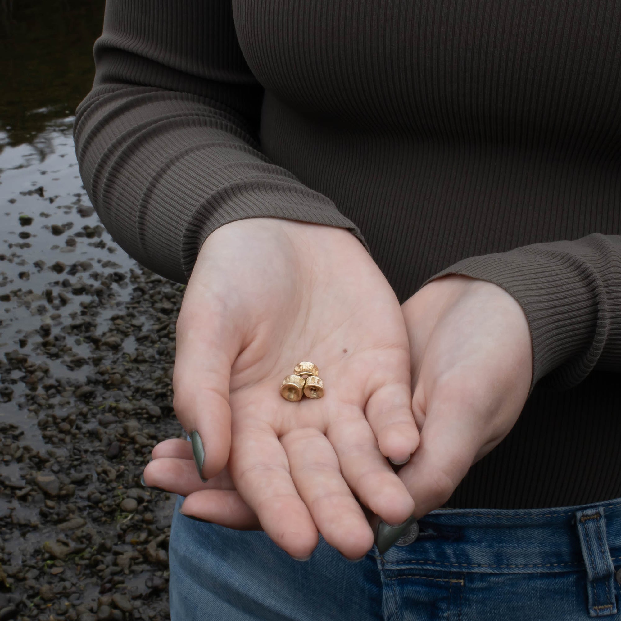 Person holding three small 10k Gold Salmon bone Vertebrae by Morgan Asoyuf in their hands with a natural background