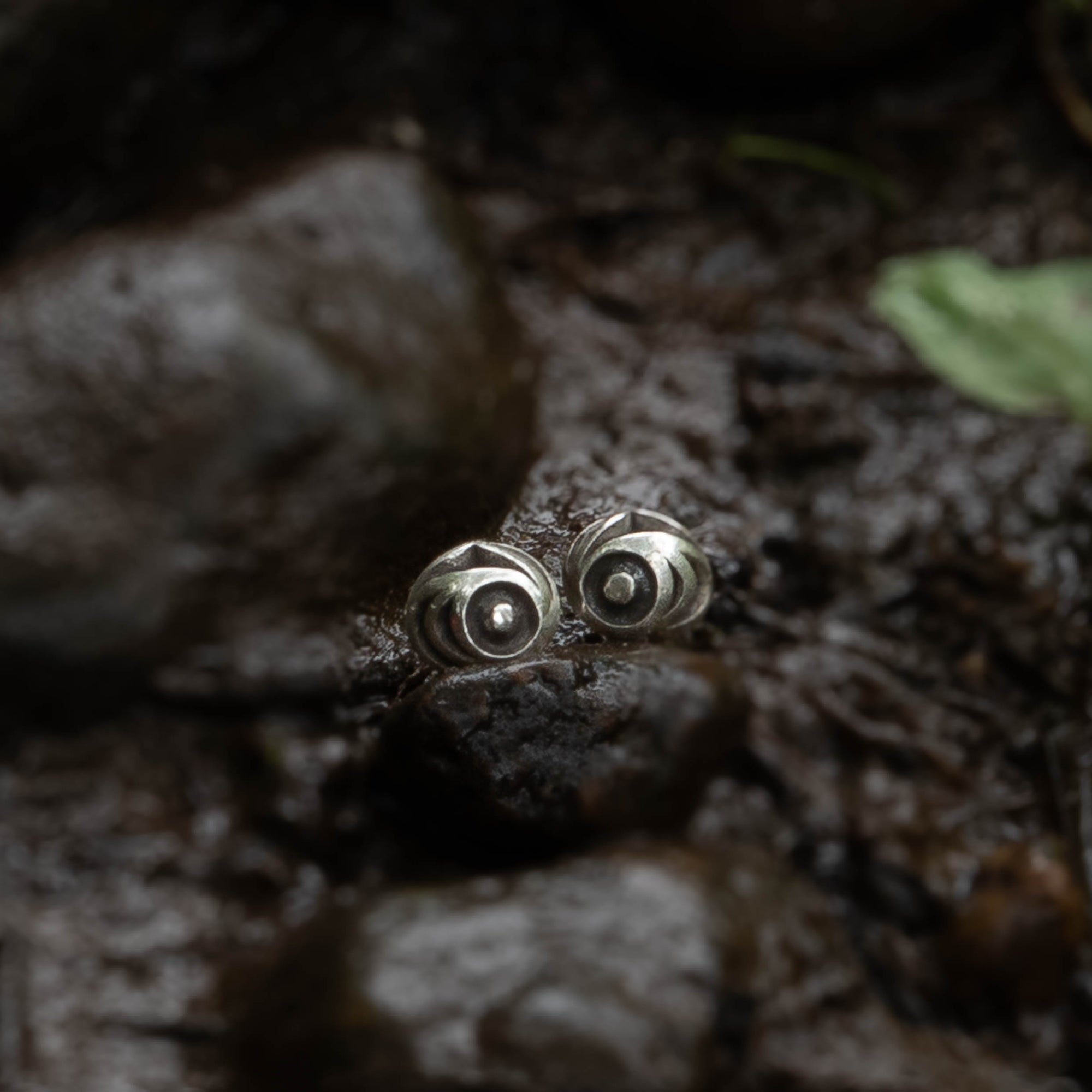 Pair of silver salmon egg earrings with black and white pattern by Indigenous Canadian Artist Meaghan Mcrae on a wet stone with water and rocks in the background