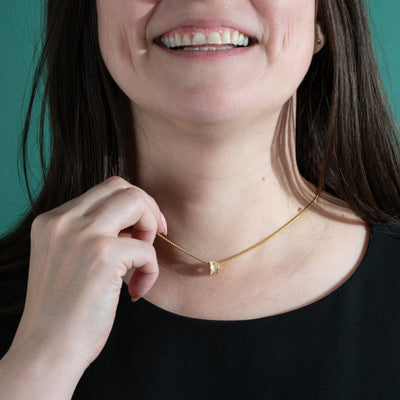 Person wearing a gold salmon bone necklace necklace with a small square pendant against a teal background