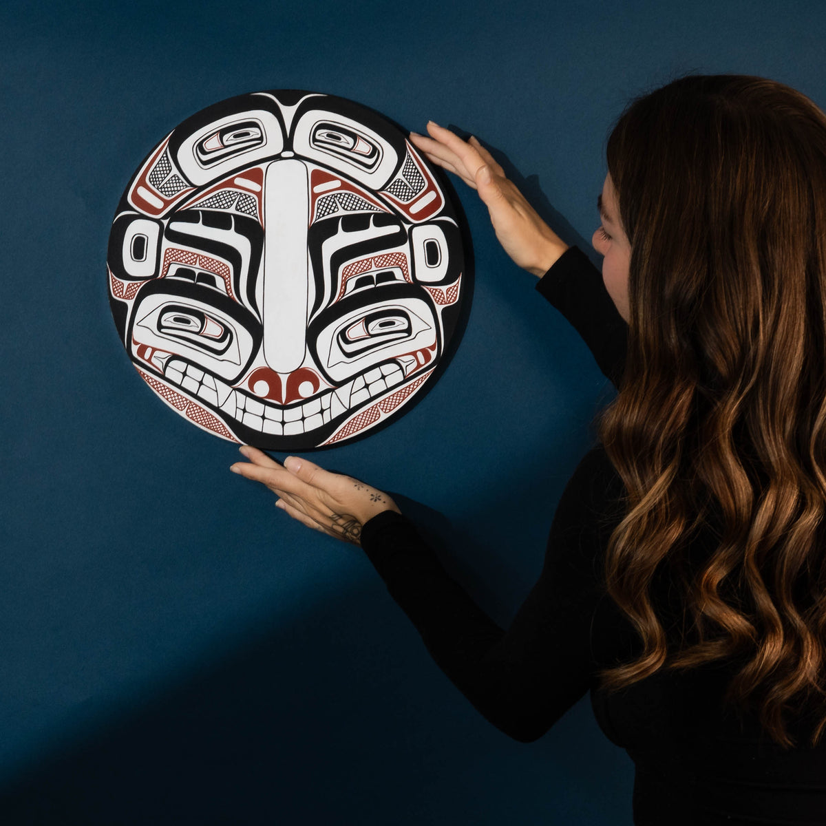 Woman holding a round, intricately designed art piece against a dark blue background