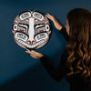 Woman holding a round, intricately designed art piece against a dark blue background