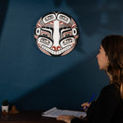 Woman sitting at a desk with a decorative mask on the wall behind her