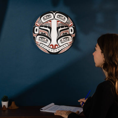 Woman sitting at a desk with a decorative mask on the wall behind her