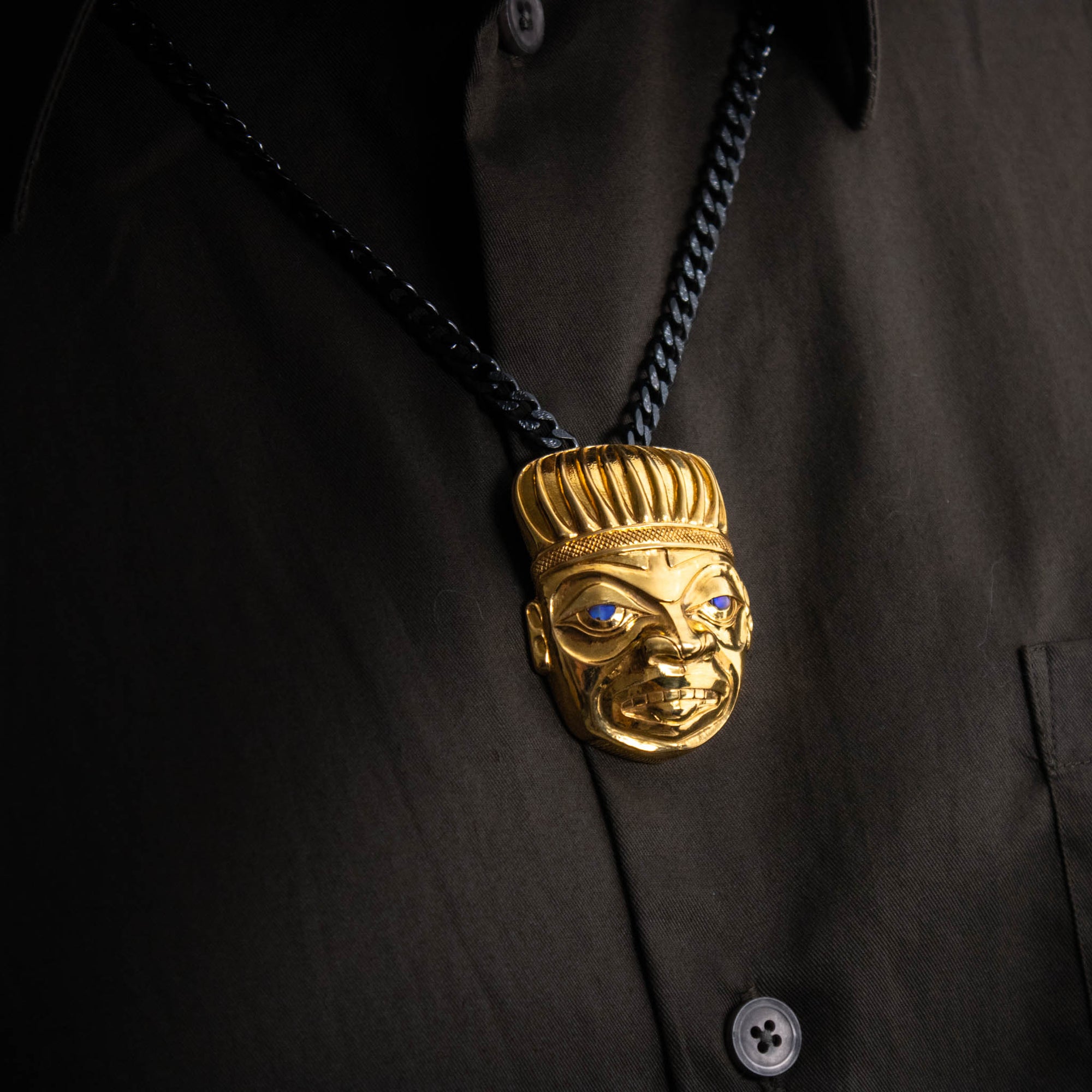 Gold Shaman pendant on a black chain worn by a model with a brown shirt and buttons