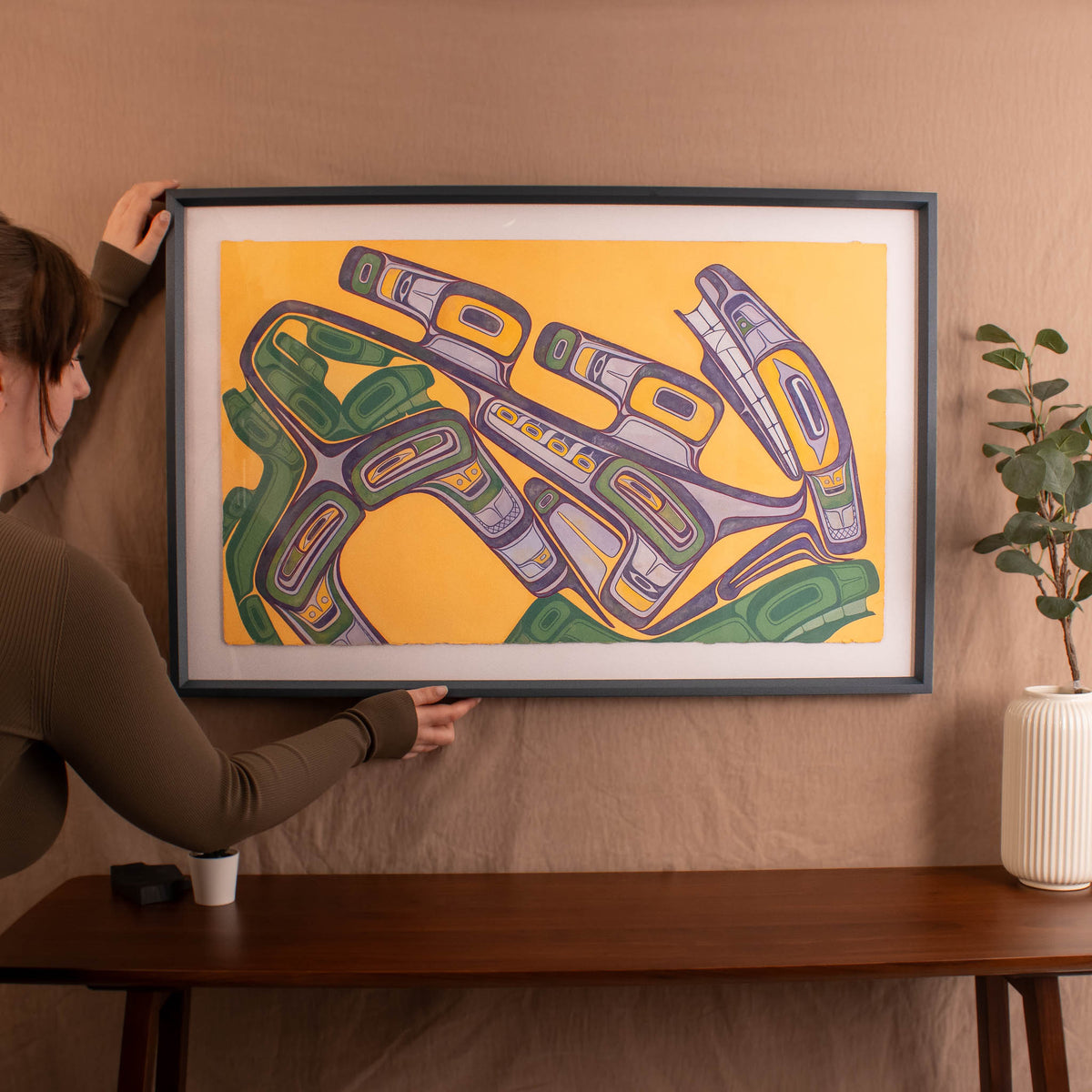 Person hanging a framed abstract artwork on a wall
