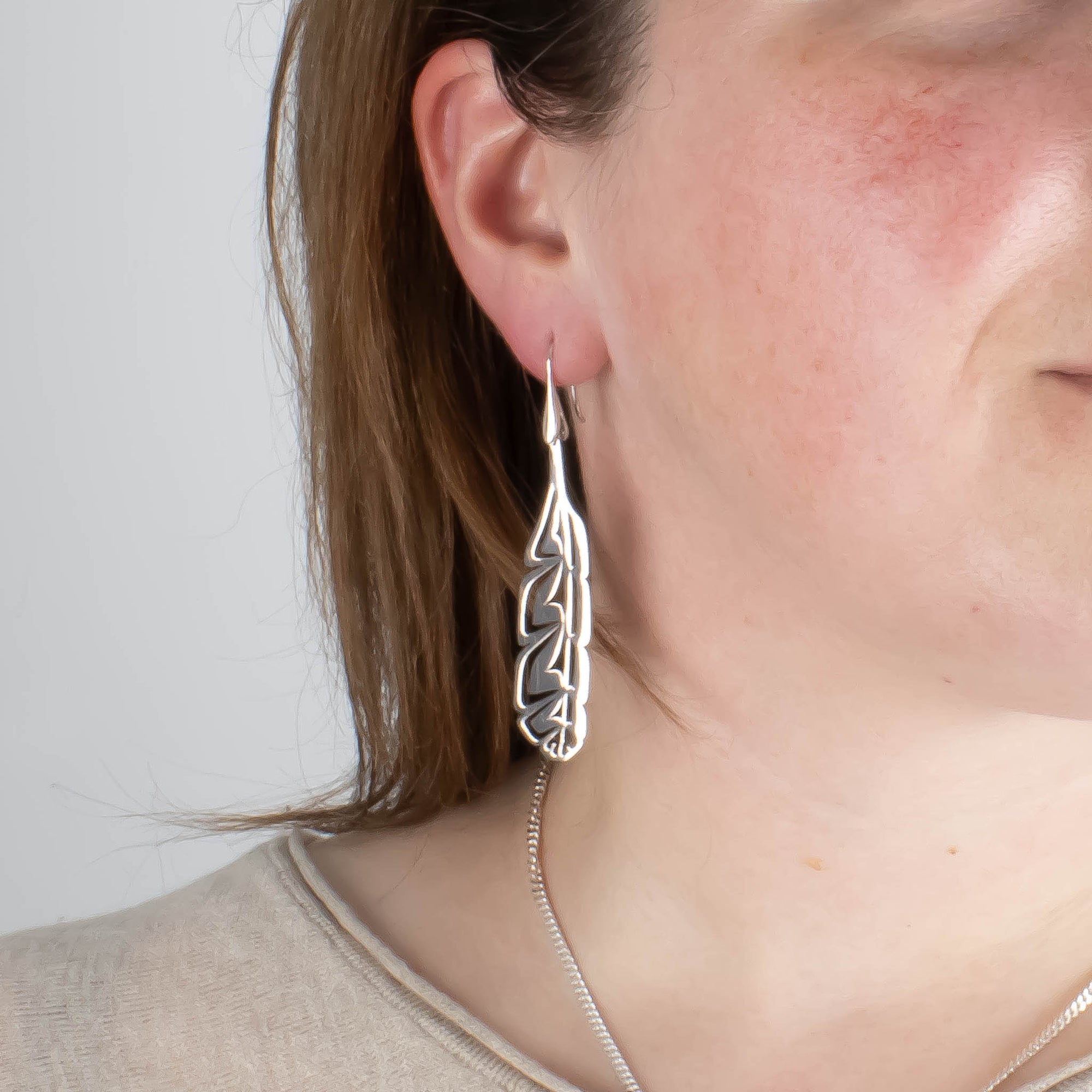 Close-up of model wearing sterling silver feather earrings and a chain