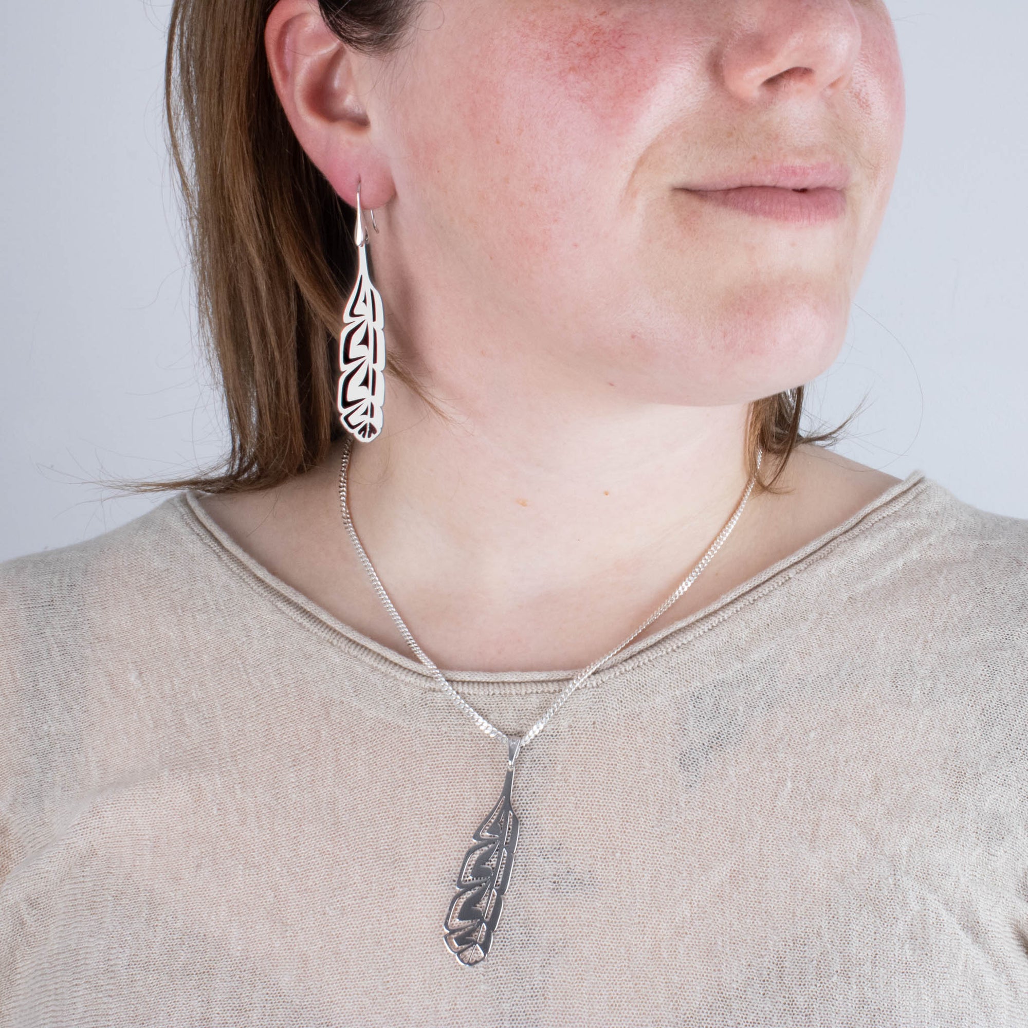 Model wearing sterling silver northwest coast formline feather earrings and pendant with a beige top