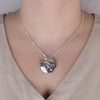 Model wearing round sterling silver engraved pendant with hummingbird design and beige shirt
