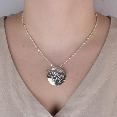 Model wearing round sterling silver engraved pendant with hummingbird design and beige shirt