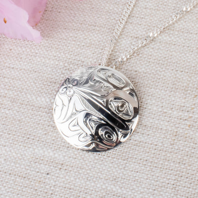 Closeup of sterling silver northwest coast hummingbird pendant and chain with pink flower in the corner