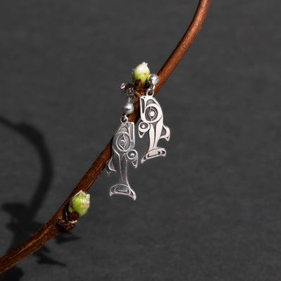 Silver salmon stud earrings dangling from a blossoms on a twig on it on a dark gray background.