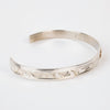 Side view of mountains on Sterling silver Bracelet featuring  14k gold formline raven head, with mountains and trees hand carved around the bracelet