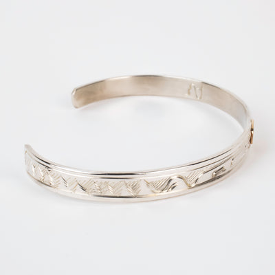 Side view of mountains on Sterling silver Bracelet featuring  14k gold formline raven head, with mountains and trees hand carved around the bracelet