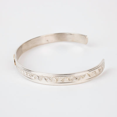 Side view of mountains on Sterling silver Bracelet featuring  14k gold formline raven head, with mountains and trees hand carved around the bracelet