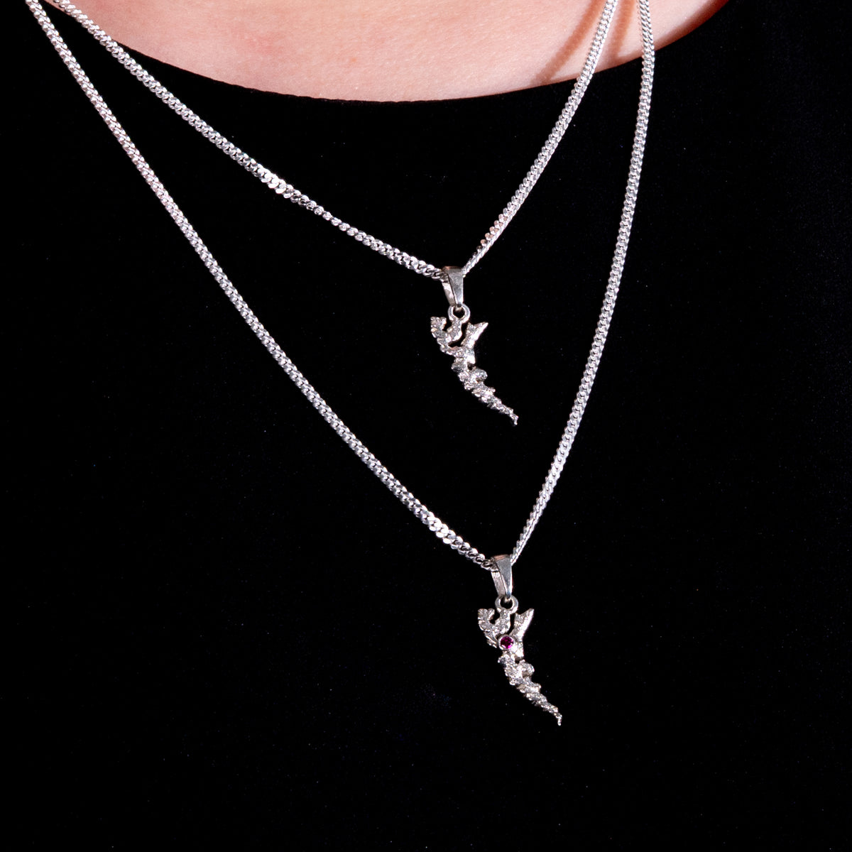 Two sterling silver island pendants layered against a black shirt. 