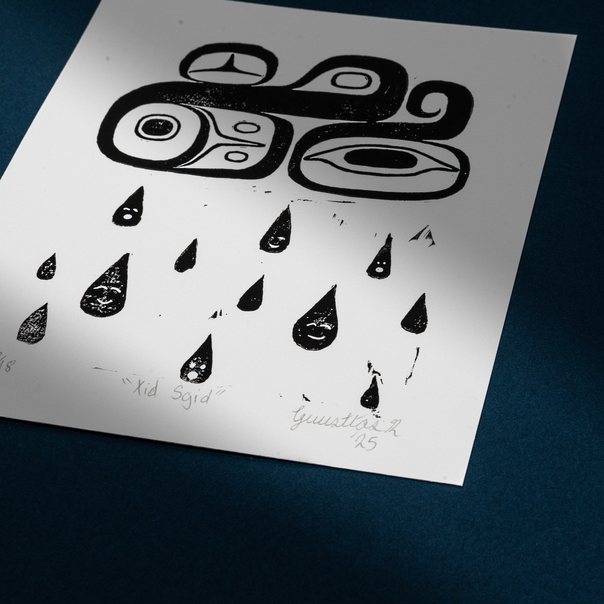 Black and white abstract Haida design of a cloud on a white art print against a dark blue background showcasing the artists original signature