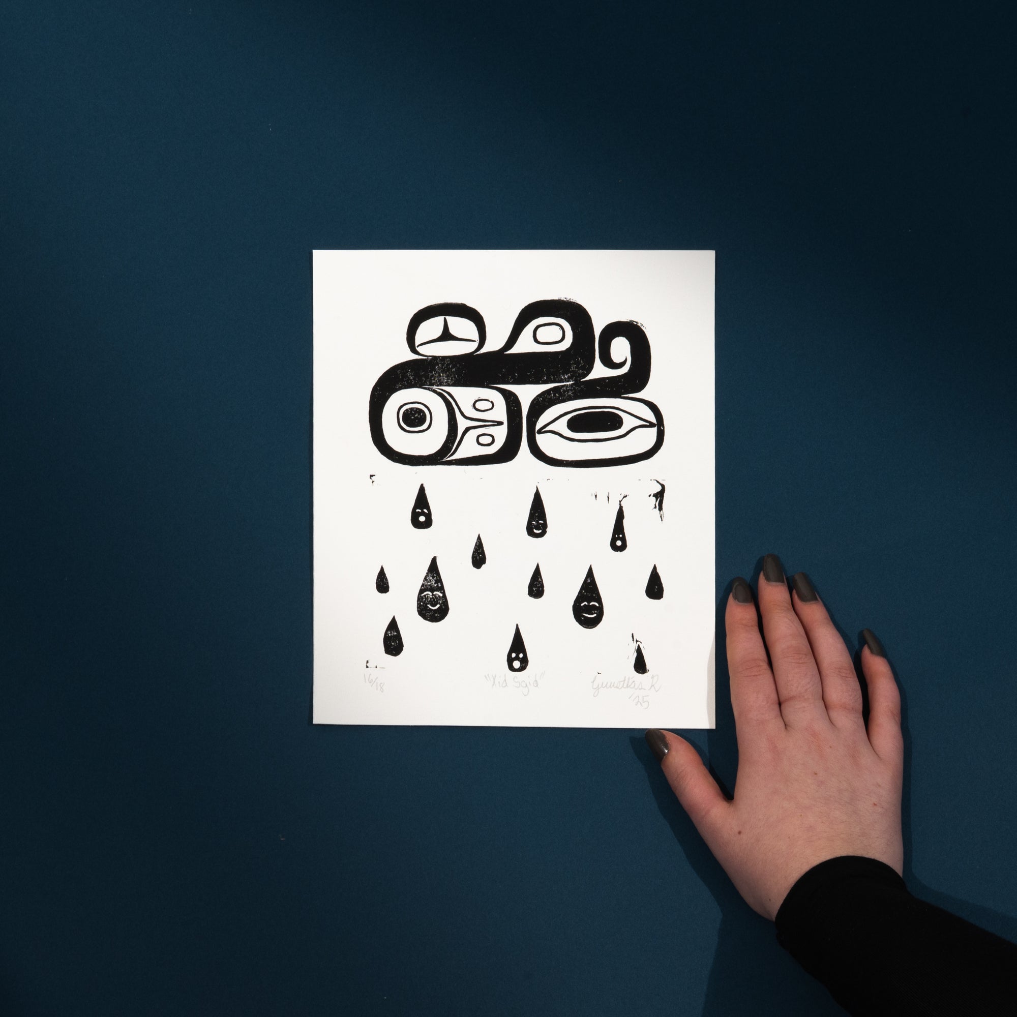 White art print with black abstract Haiart on a dark blue background, touched by a hand.a