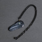 A dark charcoal gray carved raven pendant  with a black chain, displayed on a textured gray background.