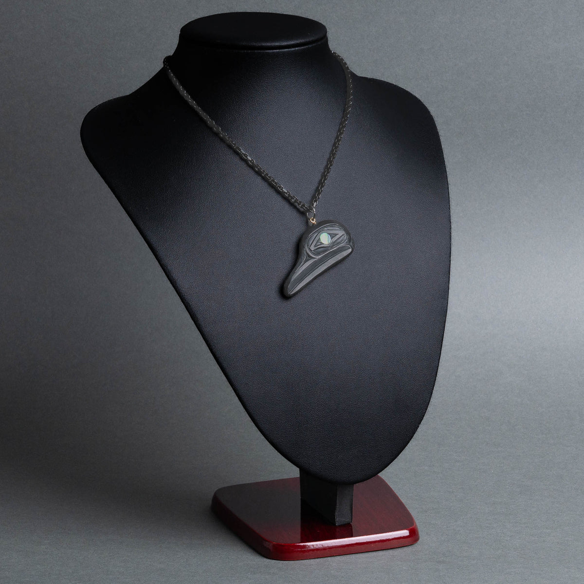 A black flicker pendant displayed on a black jewelry bust with a  soft lighting photographed against a smooth gray studio background.
