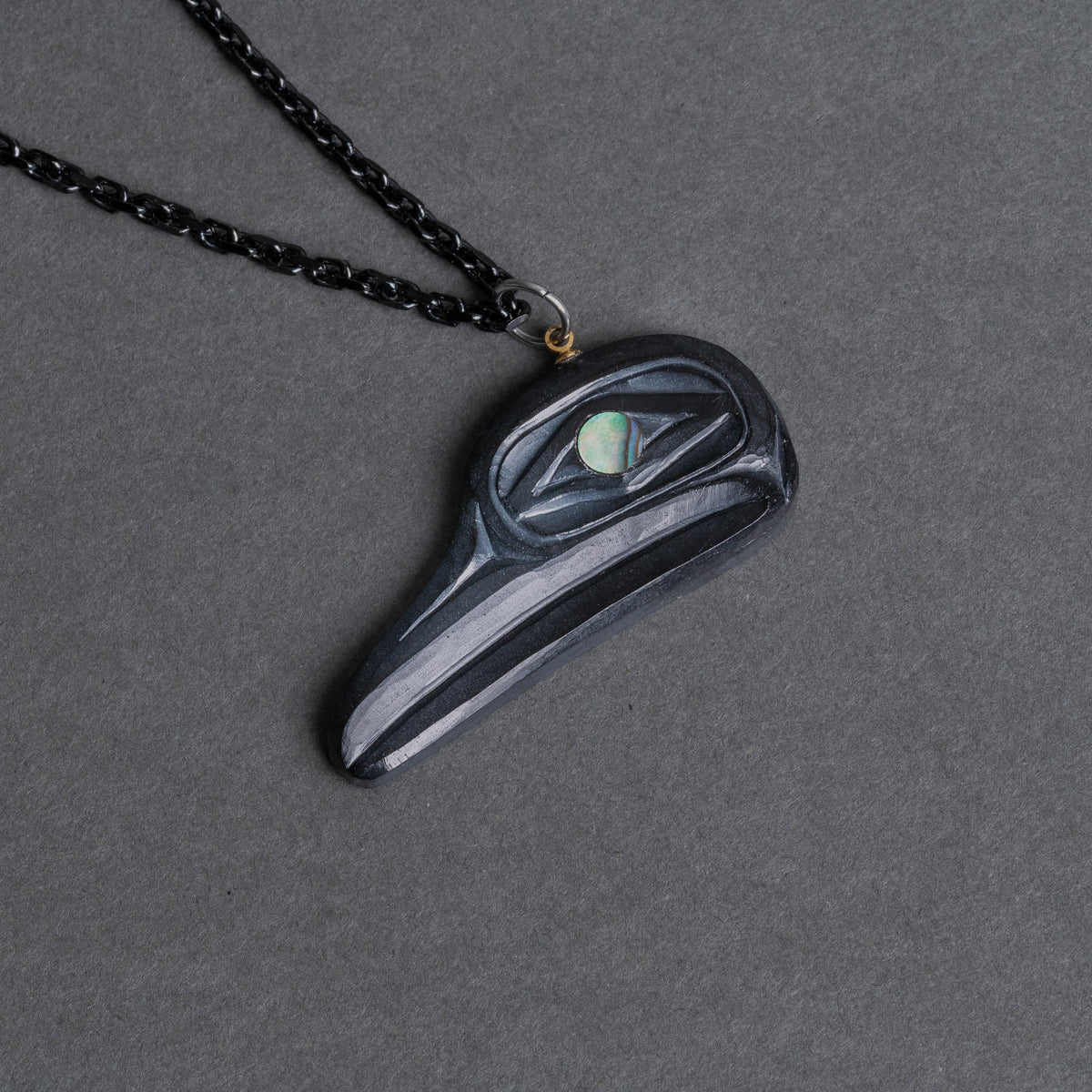 Haida Argillite Carving Flicker Bird Pendant with abalone eye and black chain by Sean Brennan on a dark grey background.