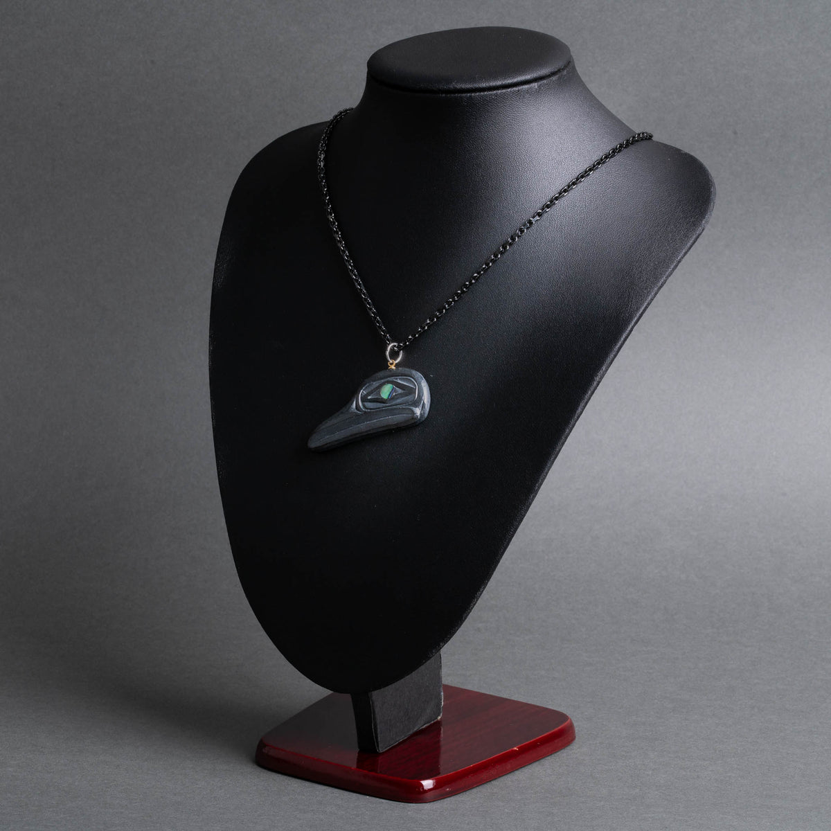 A black pendant displayed on a black jewelry bust with a dark red base, photographed against a smooth gray studio background.