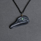 A black flicker pendant necklace with a small iridescent green eye detail, shown on a dark gray textured background.