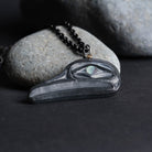 Close up of argillite flicker pendant showing its depth, proped against a ight grey rock on a dark grey background.