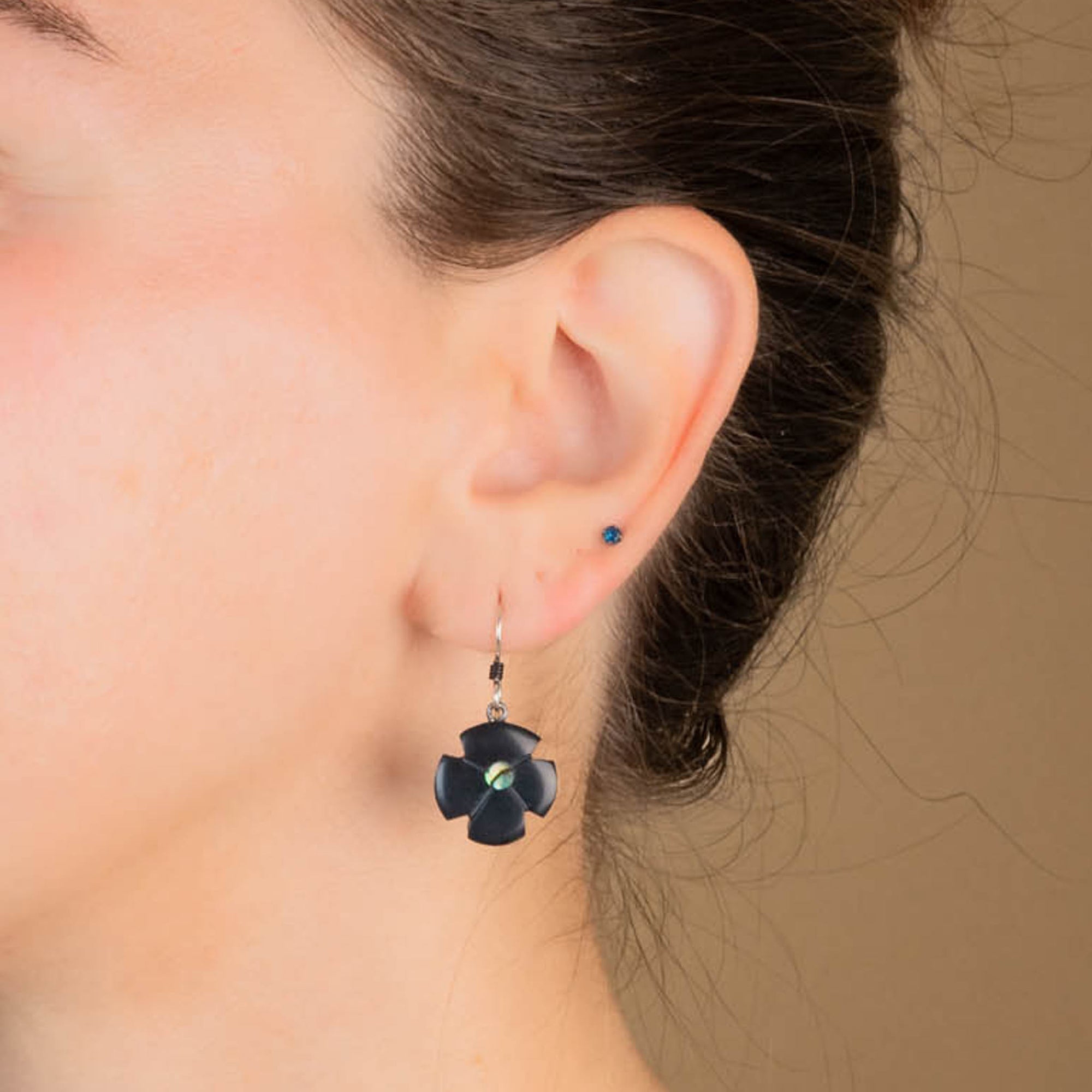 Close-up of an ear wearing a black flower-shaped earring and blue stud with a blurred background.