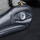 close up of a abalone eye on a block carving, with a brass loop on a black background
