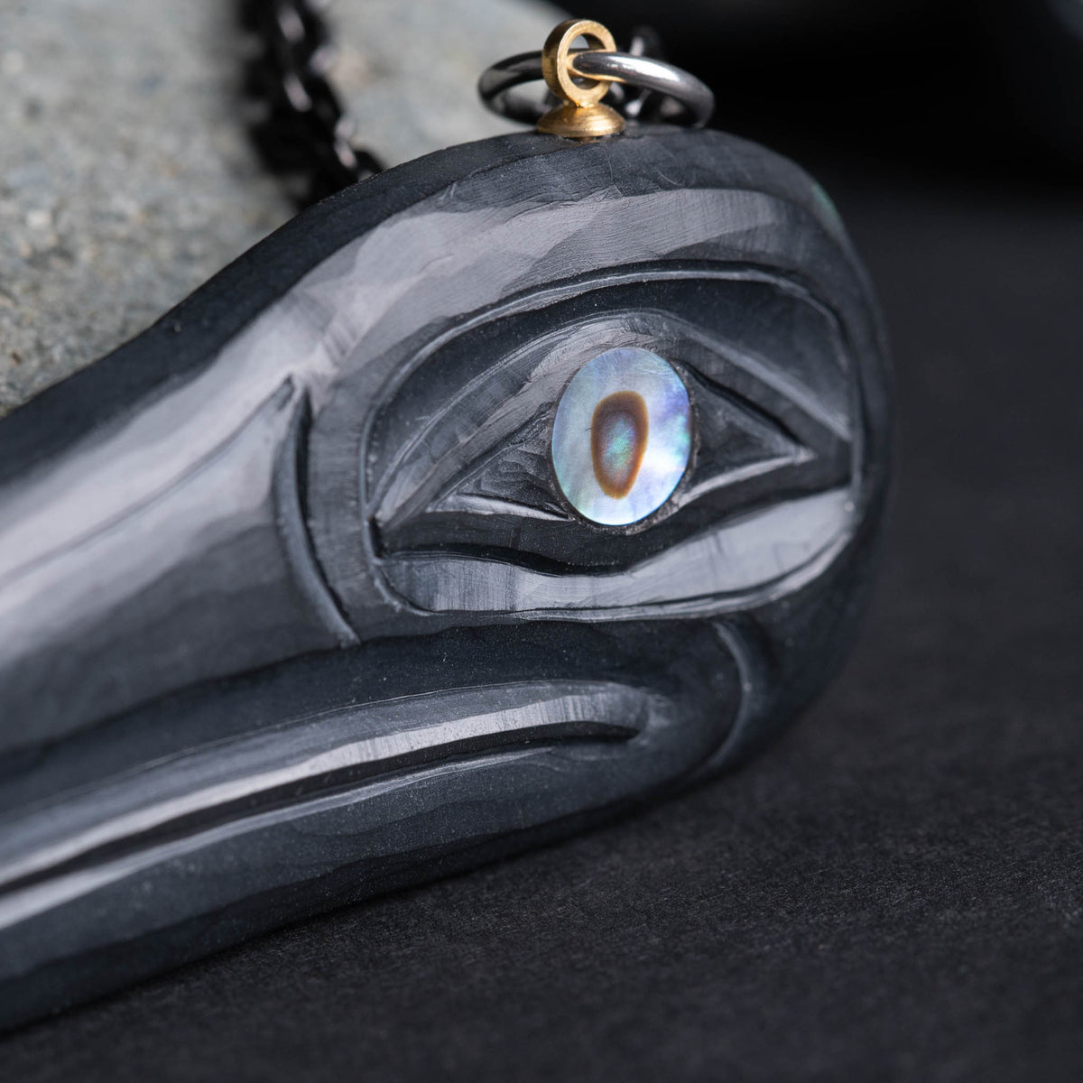 close up of a abalone eye on a block carving, with a brass loop on a black background
