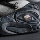 close up of hand tool marks on argillite thunderbird carving, with an abalone eye on a light and dark grey background. 