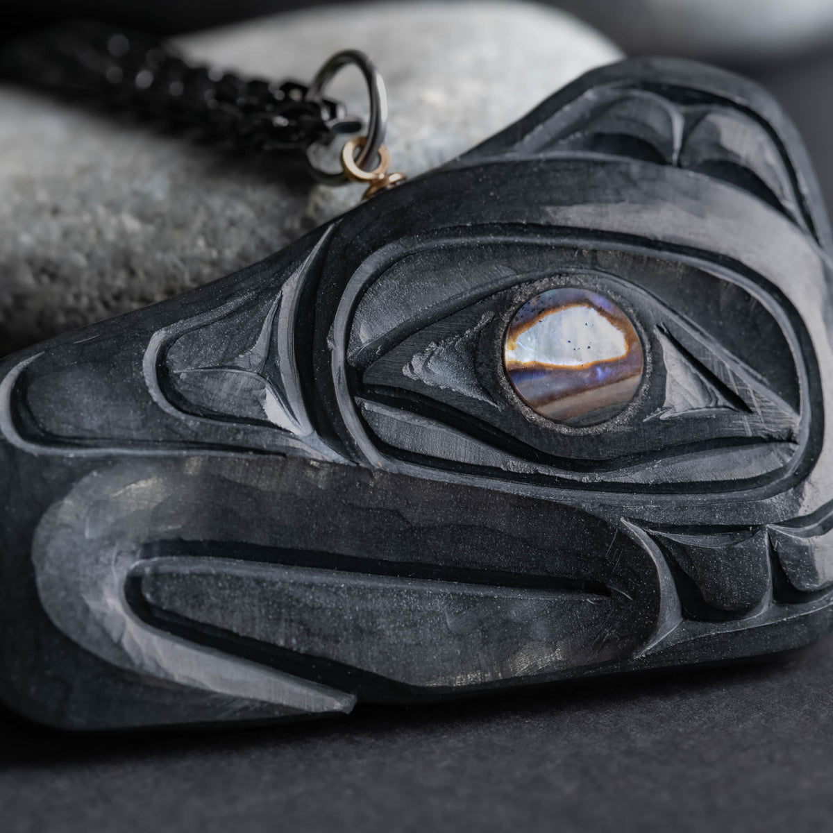 close up of hand tool marks on argillite thunderbird carving, with an abalone eye on a light and dark grey background. 