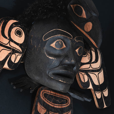 Close up of a mask with a black face and a raven head on top.