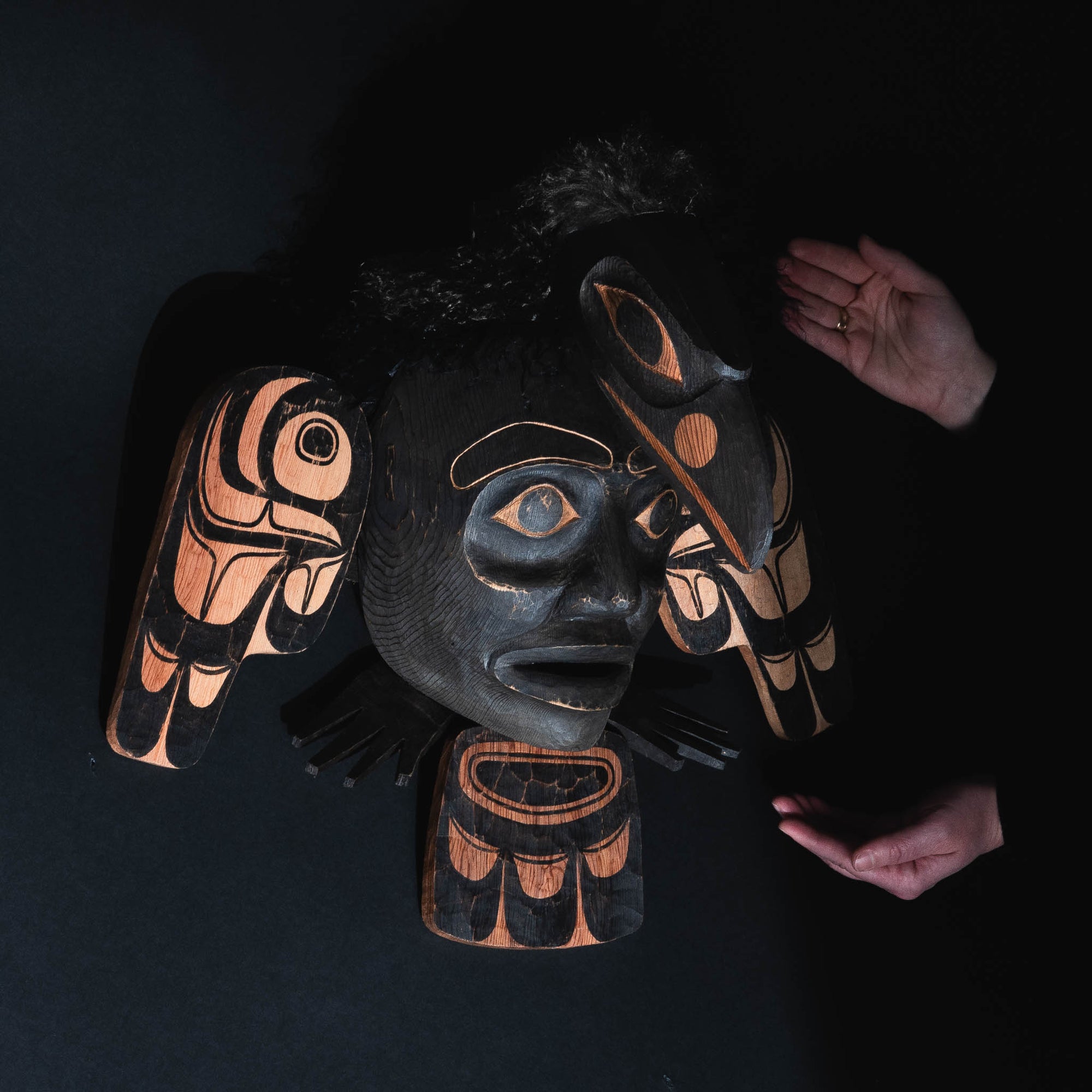 Two hands holding a wood mask with black paint.