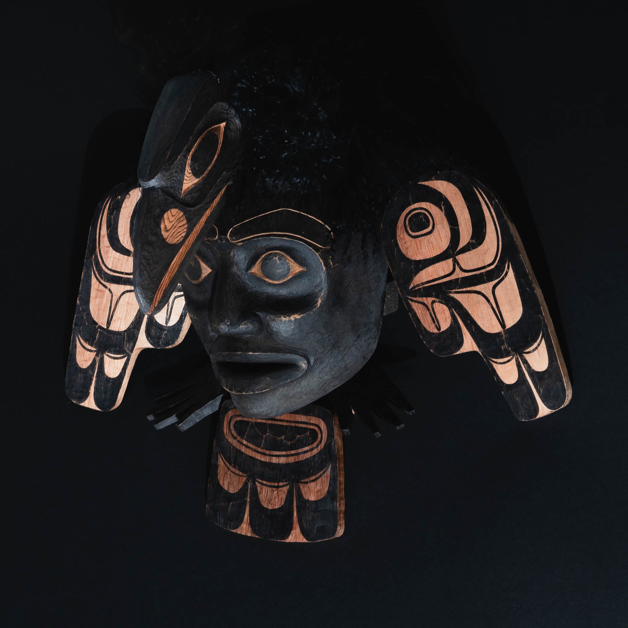 Carved black raven mask with wings and a face on a black background.