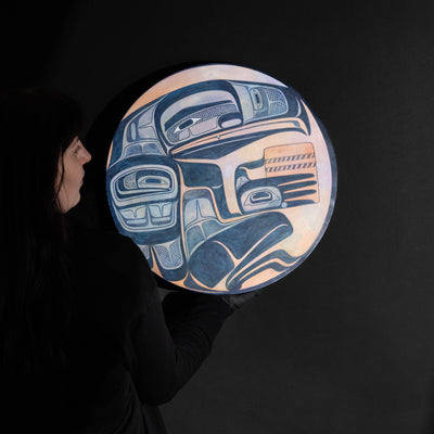 Person holding round painted panel with a figure holding a basket in blue, purple, and, orange.