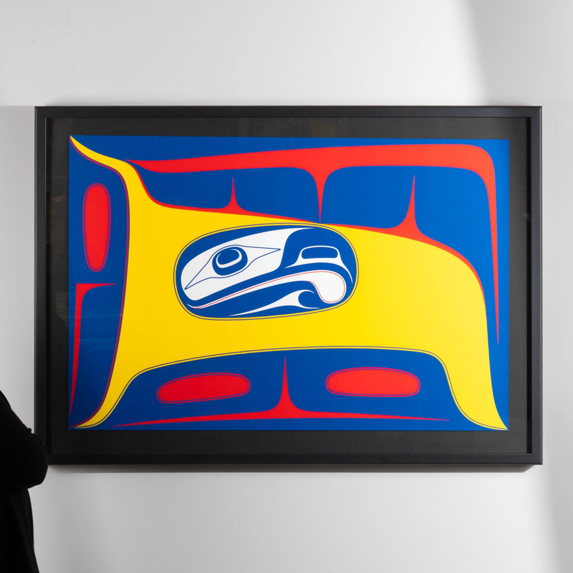 Framed Bird in the Air limited art print by Haida artist Robert Davidson on a white wall with a cropped model on the left.