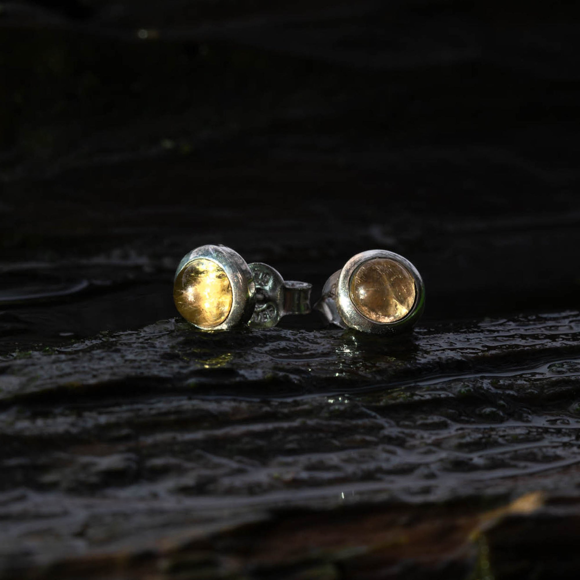 Close-up of yellow citrine sterling silver studs on a dark background
