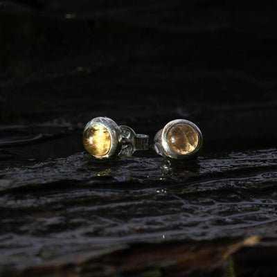 Close-up of yellow citrine sterling silver studs on a dark background