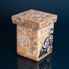 A wooden box painted showing two faces, one golden and one dark, with painted spheres around them on a dark blue background. 