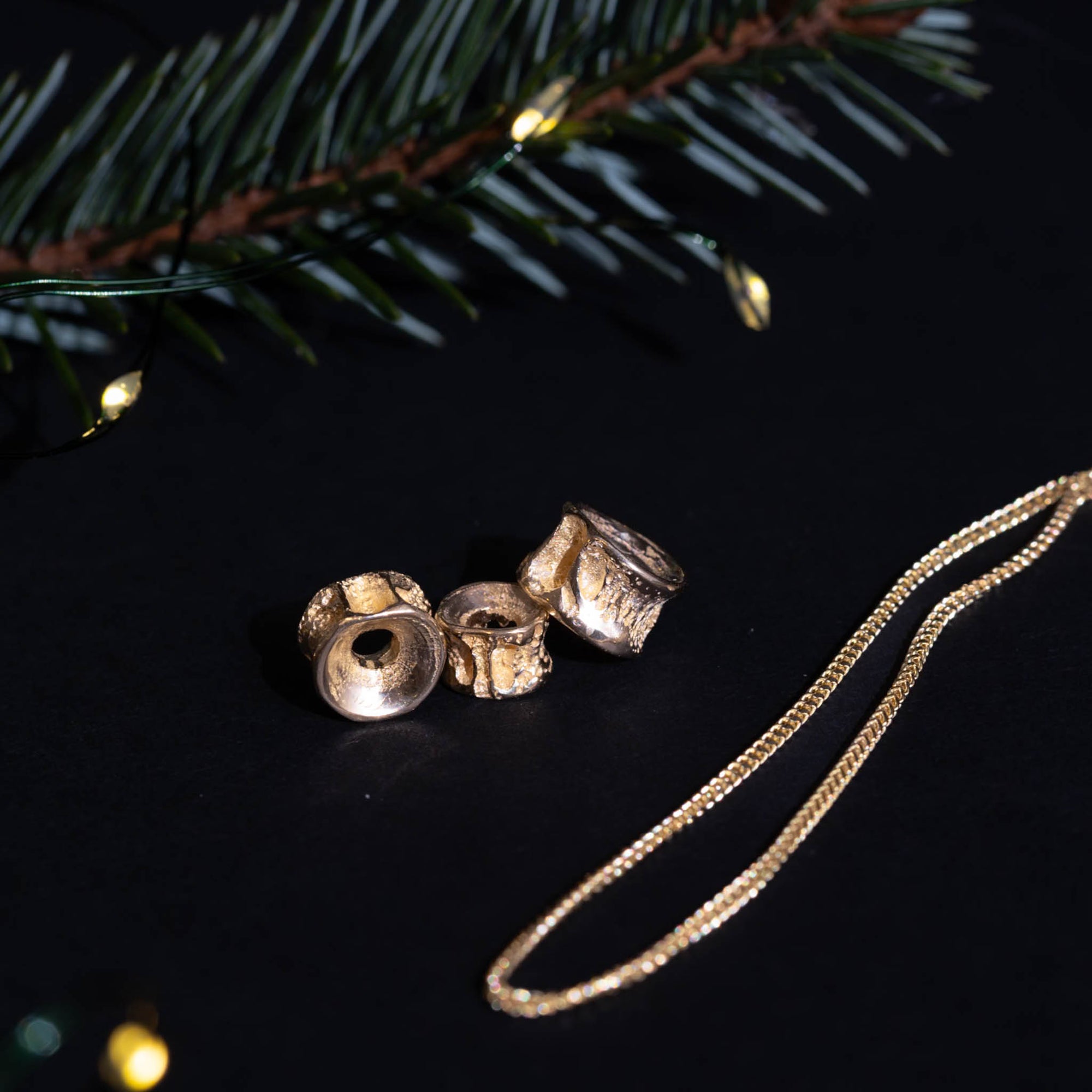 Gold necklace with three 10k gold salmon bone vertebrae charms on a dark surface with Christmas lights in the background