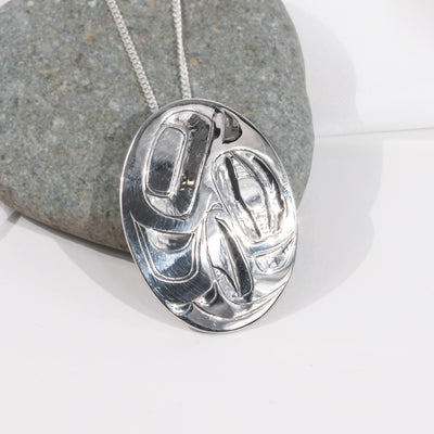 Sterling Silver haida eagle pendant  by haida jeweller Alvin Adkins on a chain against a stone background