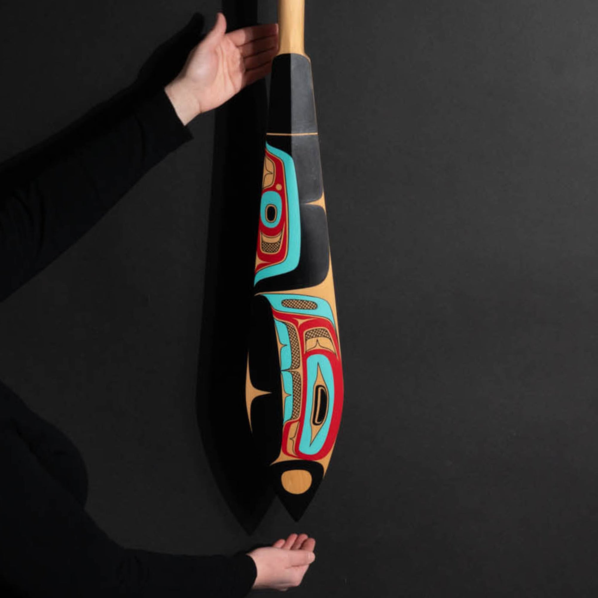 Decorative paddle with colorful patterns held by a person on the left side against a black background