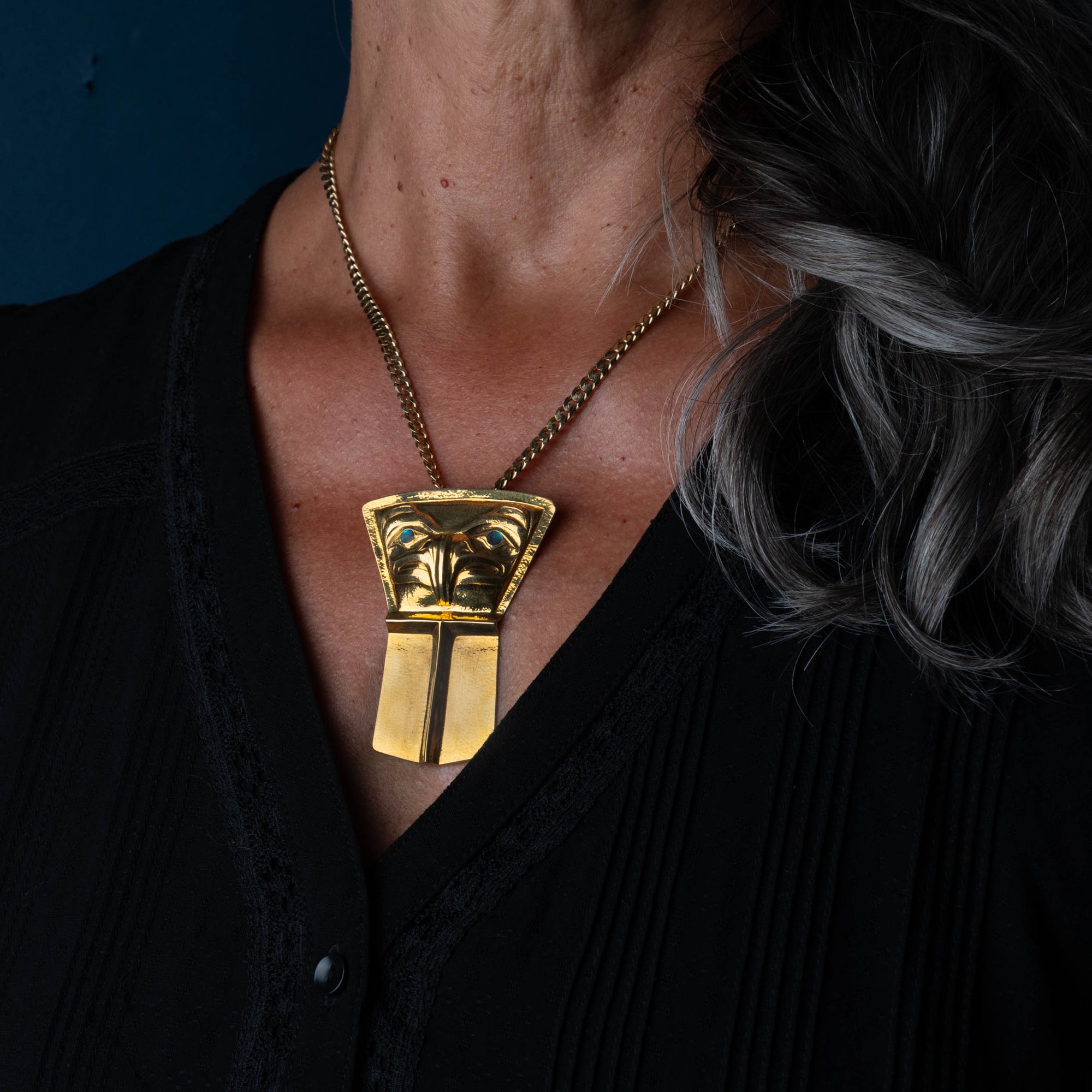A woman wears a gold pendant and chain in the shape of an eagle and shield with blue eyes