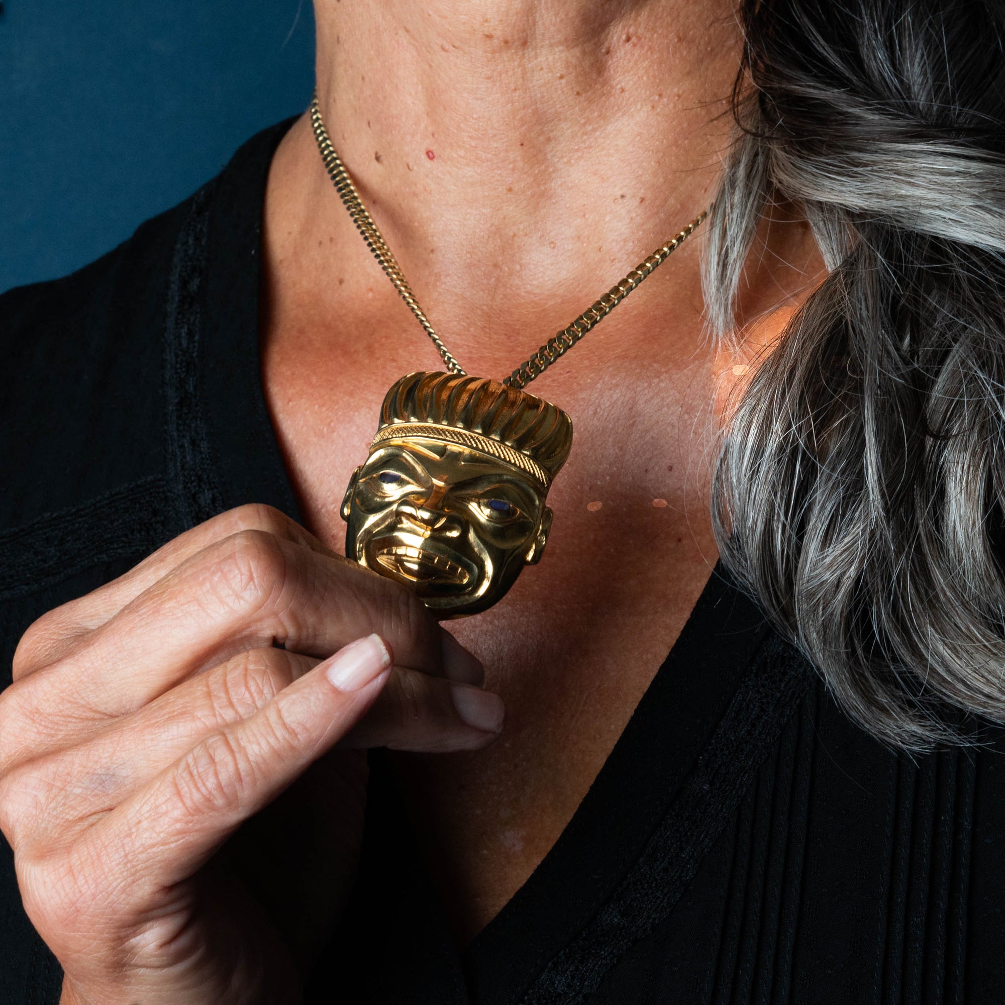A woman model holding a gold pendant with her hand, while modelling the pendant
