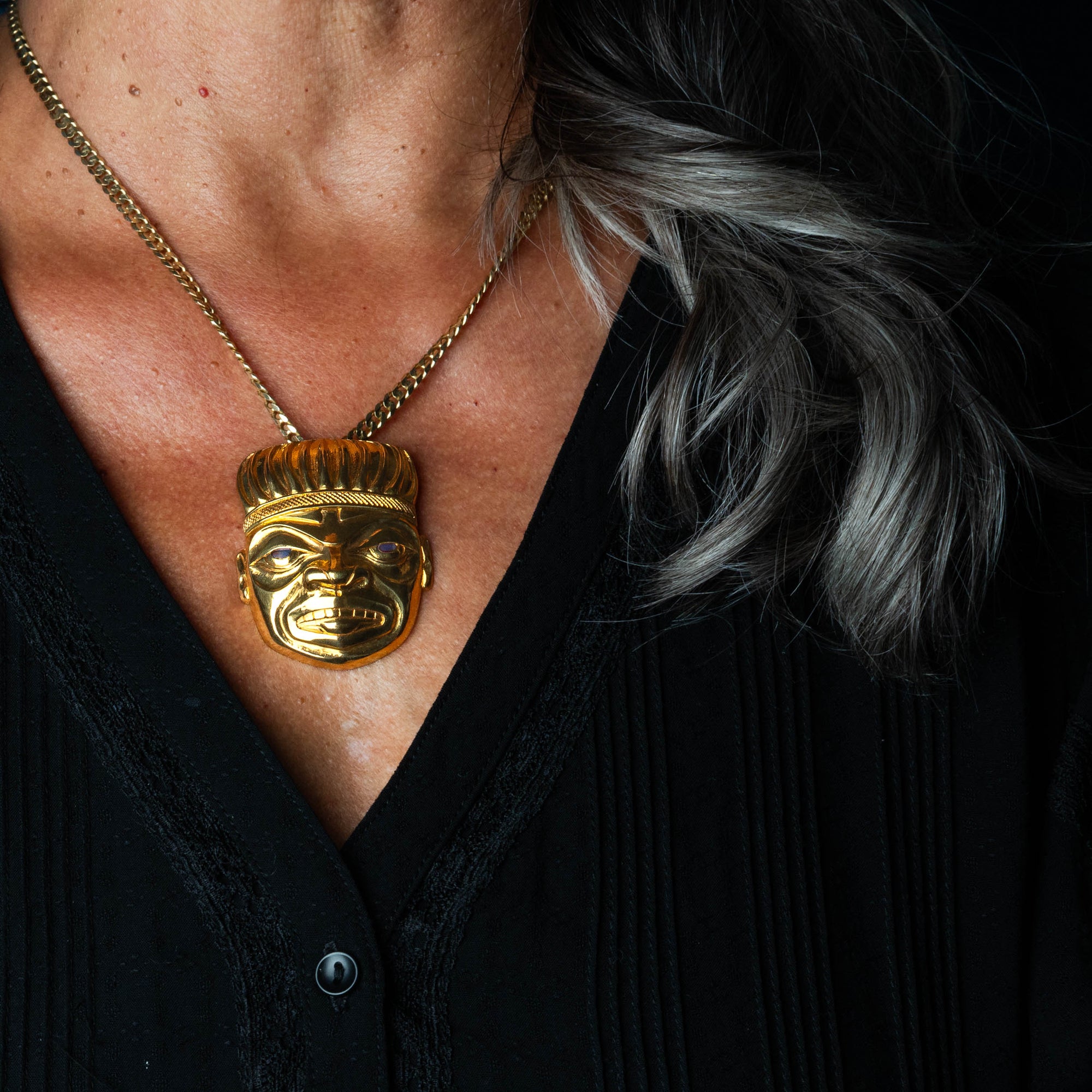 Gold pendant with chain worn by a woman with a black shirt