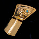 A close-up of a gold pendant in the shape of a shield on a a black background